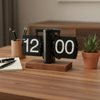 Flip clock on a wooden desk with a plant and stationery items in the background