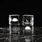 Two crystal blocks with engraved designs of a cloud, deer, and dandelion on a dark surface.
