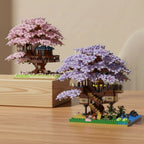 Two mini brick models of cherry blossom trees with houses on a white surface.