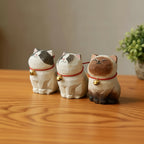 Three cat-shaped incense burners with red strings and gold bells on a wooden surface.