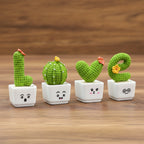 Four small cactus figures, that spell out "Love", on top of white pots, with a wooden desk background