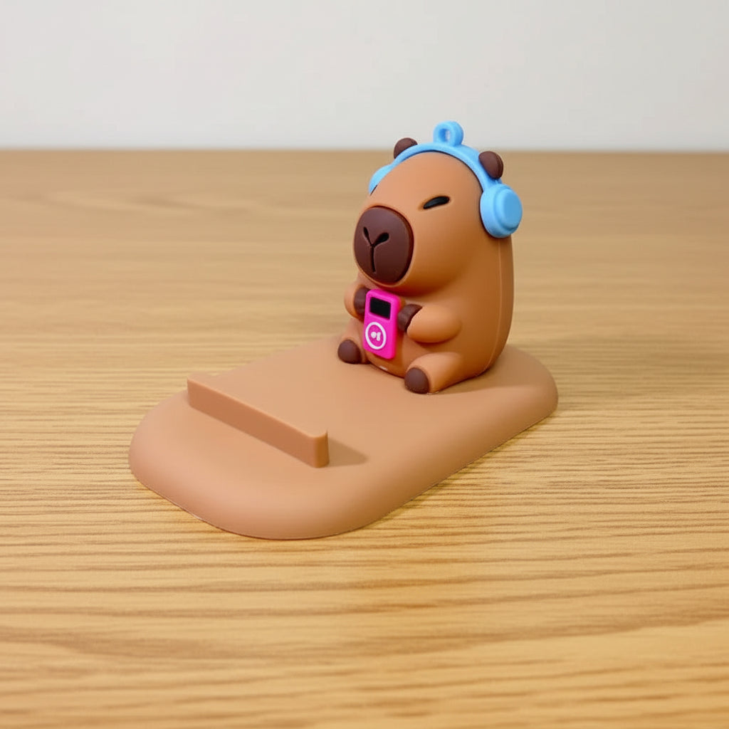capybara phone stand with blue headphones and a pink device on a gray surface.
