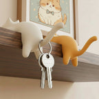 Two cat-shaped hooks on a wooden surface with keys hanging from one of them.