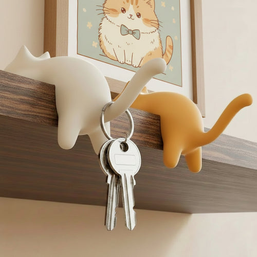 Two cat-shaped hooks on a wooden surface with keys hanging from one of them.