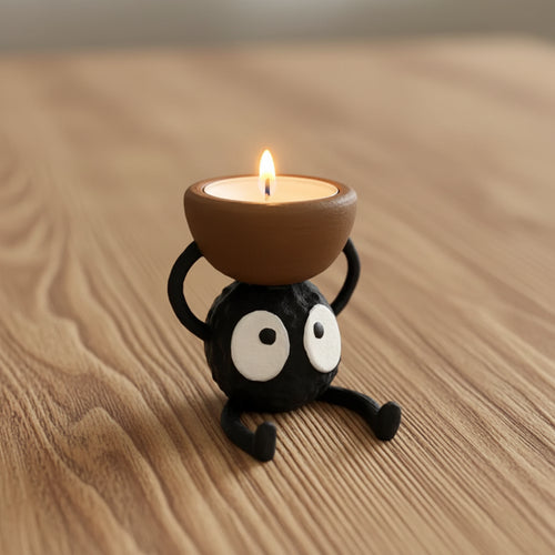 Ceramic candle holder shaped like a black cat with white eyes, holding a lit candle.