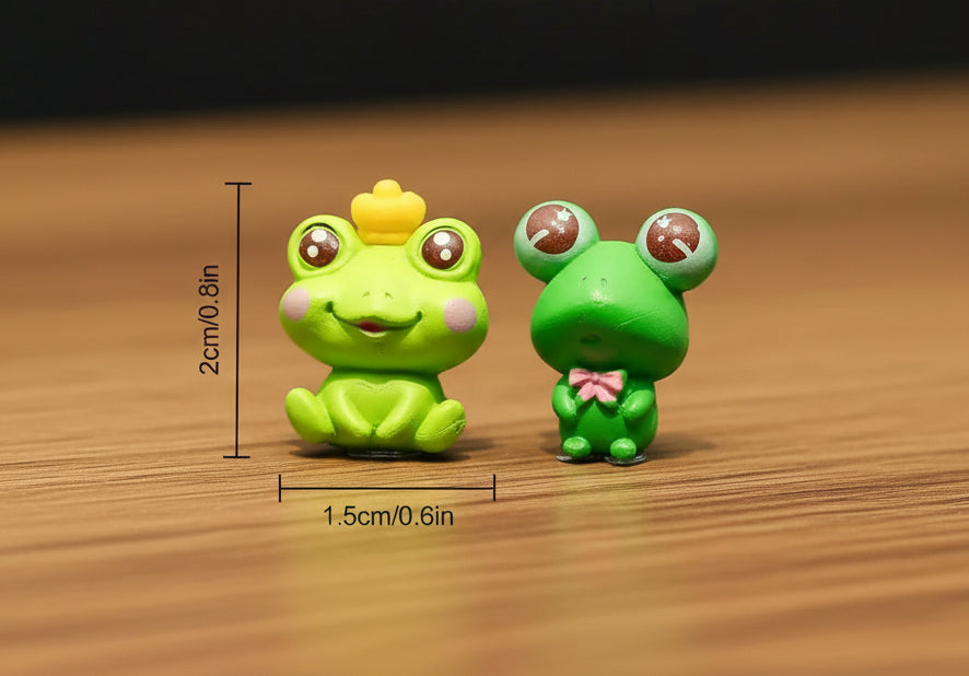 Two small green frog figurines with measurements on a gray surface.