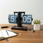 Desk setup with a unique flip  clock, notebook, pen, and small plant on a wooden surface.