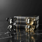 Two glass bear figurines, one silver and one gold, on a light surface with a blurred background.