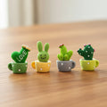 Four cute mini decorative cactus figures in colorful pots on a wooden desk
