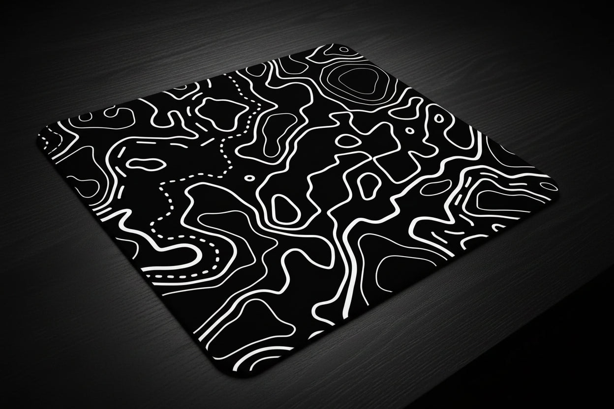 Black and white abstract patterned mouse pad on a desk with small figurines in the background.