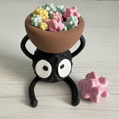 Black spider-like holder with a bowl of colorful balls on a light wooden surface