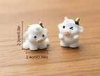 Two small cow figurines with measurements on a textured surface