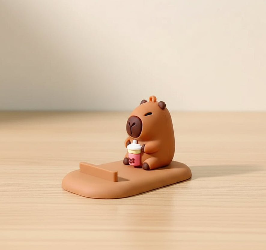 capybara phone stand  holding a cupcake on a wooden stand against a beige background