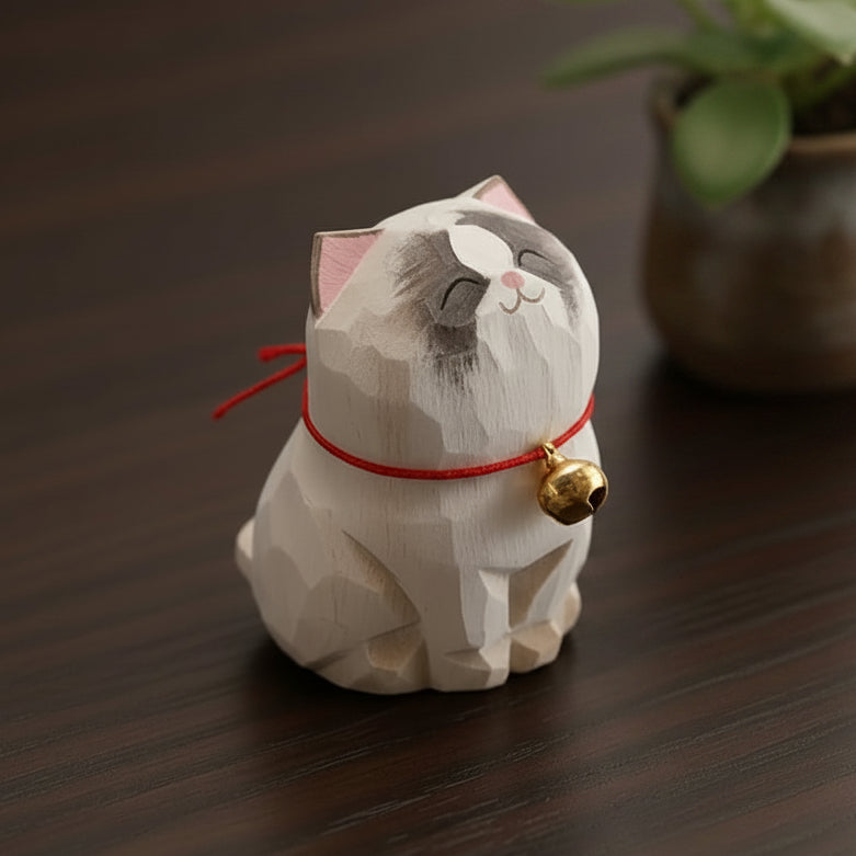 White cat figurine with a red string and gold bell on a wooden surface