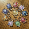 Collection of silver turtle-shaped charms with colorful sequin fillings on a white background