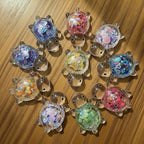 Collection of silver turtle-shaped charms with colorful sequin fillings on a white background