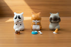 Three cat-shaped desk decorations on a car's gray dashboard with a close-up of two cat figures below.