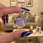 Hand holding a decorative item with colorful glitter inside, against a blurred natural background