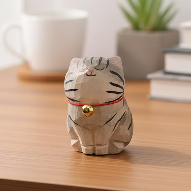 Cat-shaped decorative item with a red ribbon and gold bell on a wooden surface.