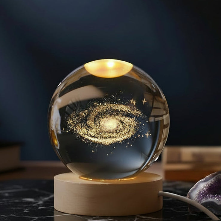 Glass sphere with galaxy design on a wooden base, illuminated against a dark background.