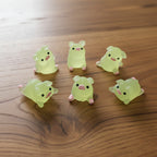 Six small green animal figurines with pink accents on a woodedn desk