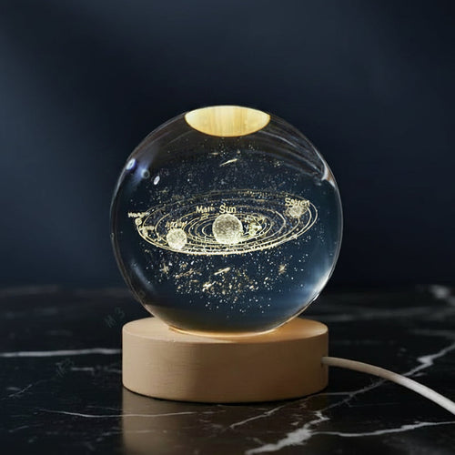 Glass sphere with solar system model on a wooden base against a dark background