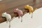Three cat-shaped desk organizers in white, pink, and yellow on a wooden surface.