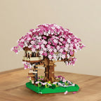 mini brick model of a treehouse with pink flowers on a wooden surface