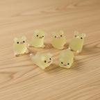Six small yellow animal figurines with pink accents on a wood table