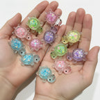 Colorful glittery turtle figurines held in white gloves on a wooden surface