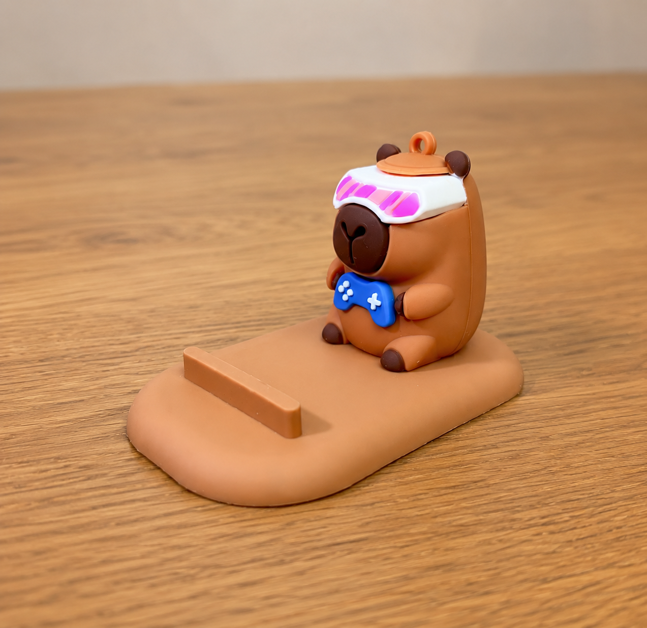 capybara phoen stand with a blue game controller on a wooden surface