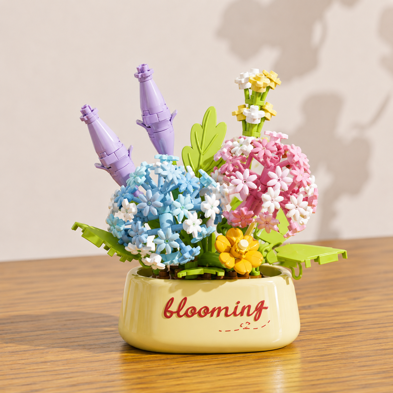 Decorative blue and pink building block flowers, in a pot labeled 'blooming', on a wooden surface.