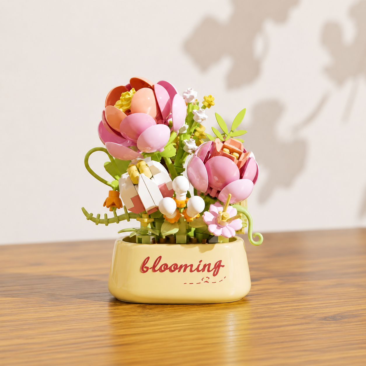 Decorative pink and white building block flowers, in a pot with 'blooming' text, on a wooden surface.